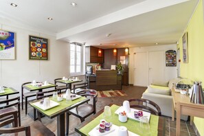 A hotel dining area with tables set for breakfast, a kitchen in the background, and a reception desk. - Hotel Le Mistral (Cannes)