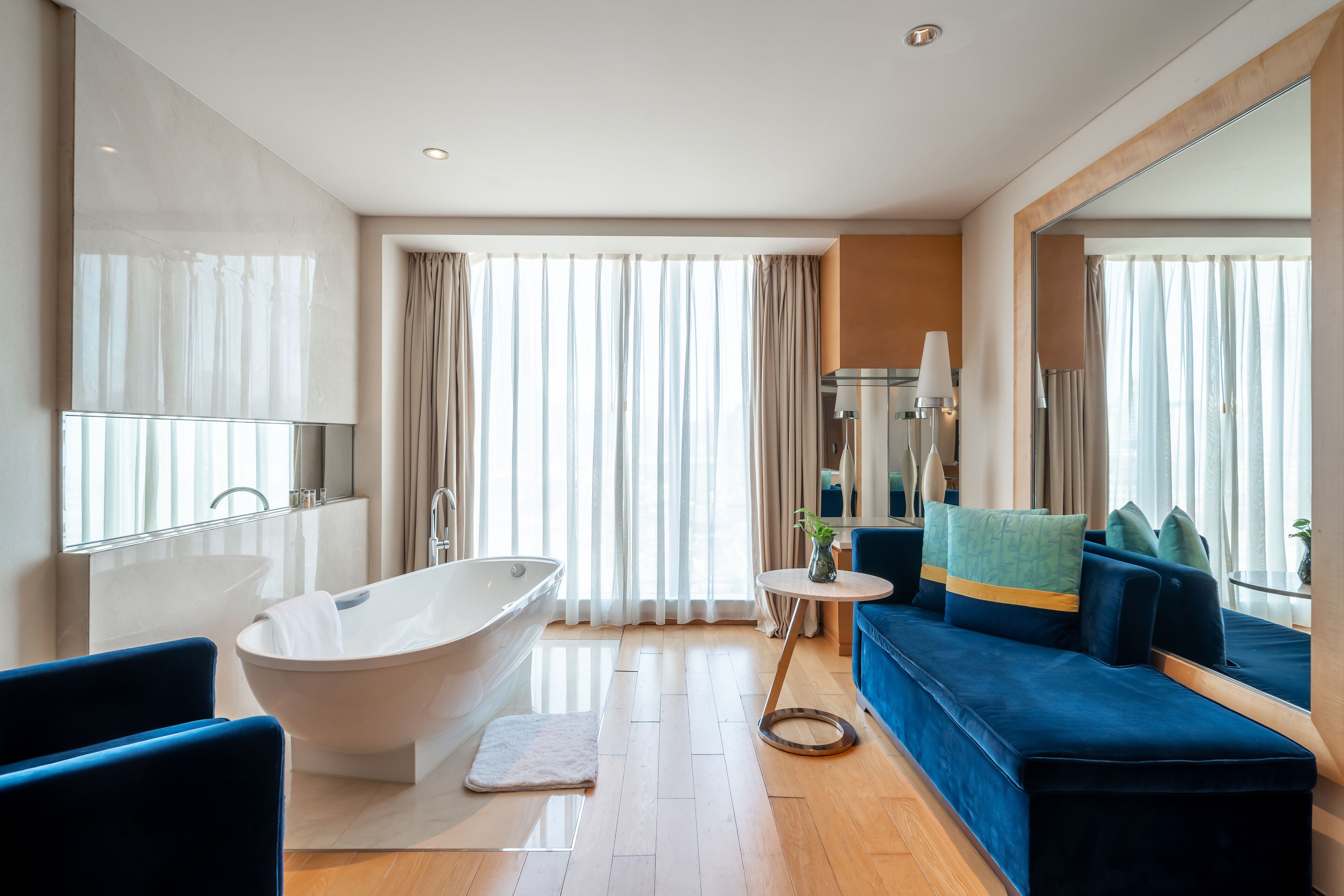 Un baño moderno con una bañera independiente, un sofá azul y una pequeña mesa redonda con un florero.