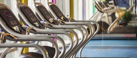 A row of stationary exercise bikes with digital displays, arranged in a gym setting.