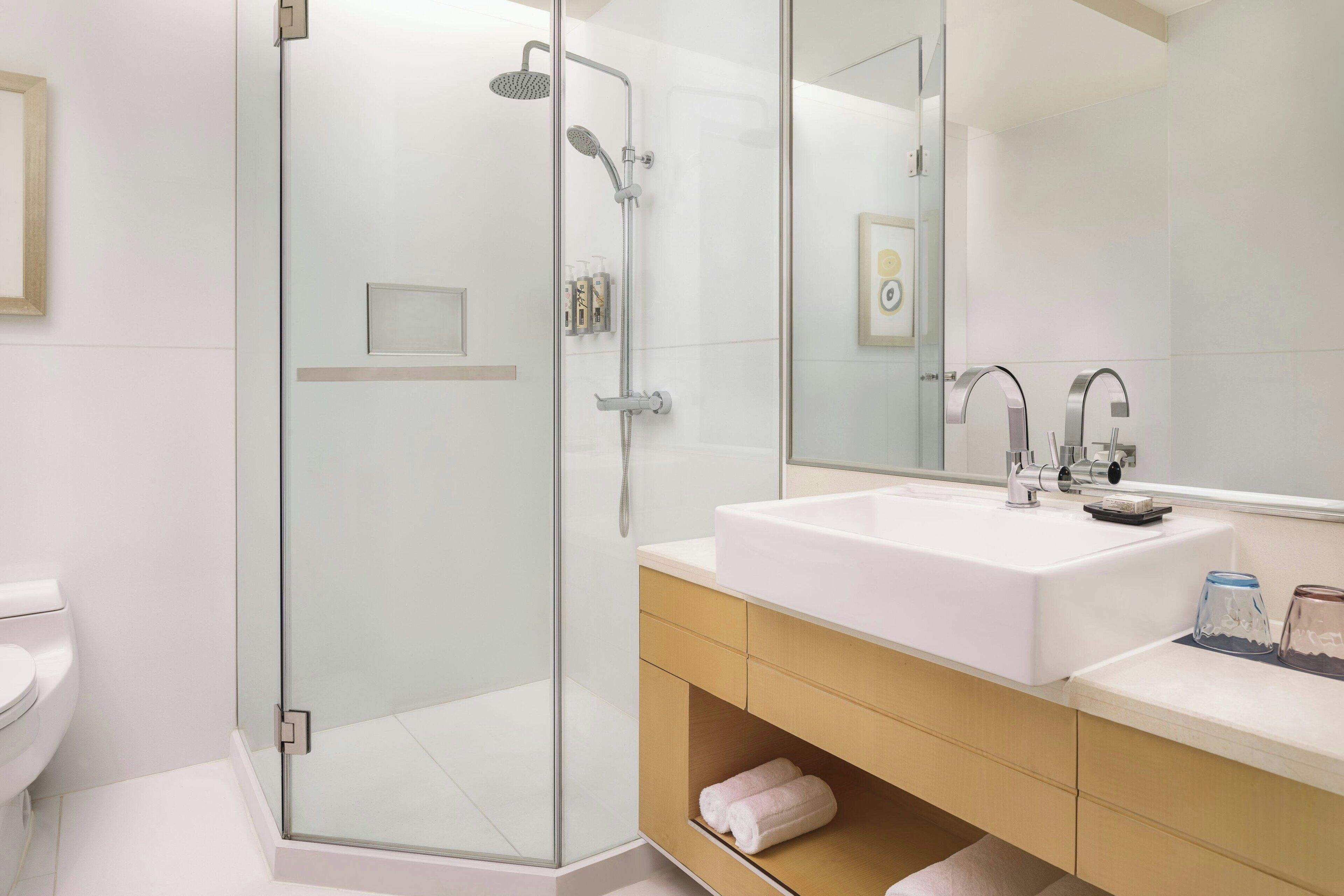 A modern bathroom with a glass-enclosed shower, a white sink, and a wooden vanity.