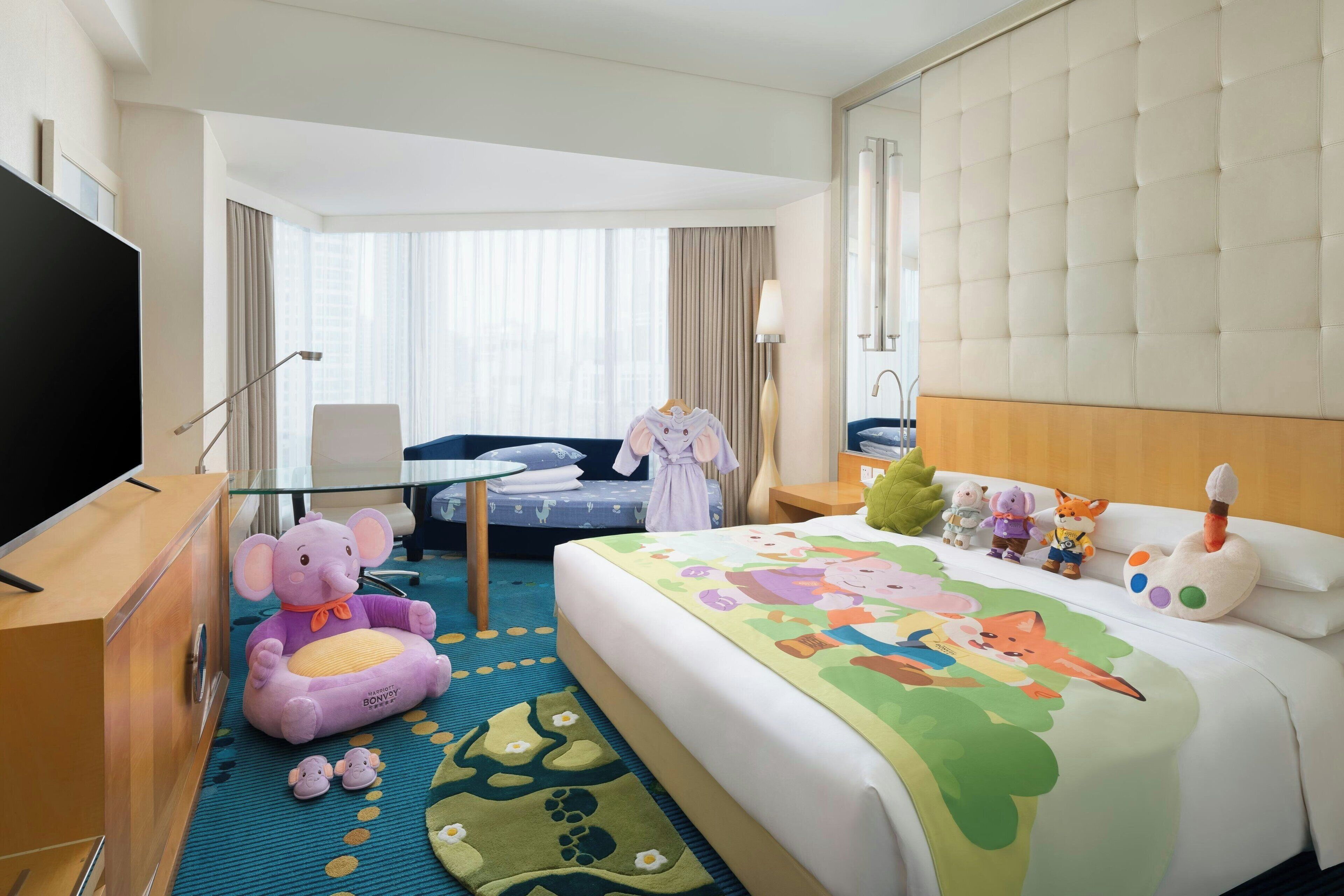A hotel room with a large bed, a desk, a television, and a plush elephant toy.