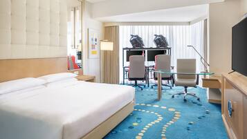 Une chambre d’hôtel avec un grand lit, un bureau avec un ordinateur, une télévision et une vue sur la ville.