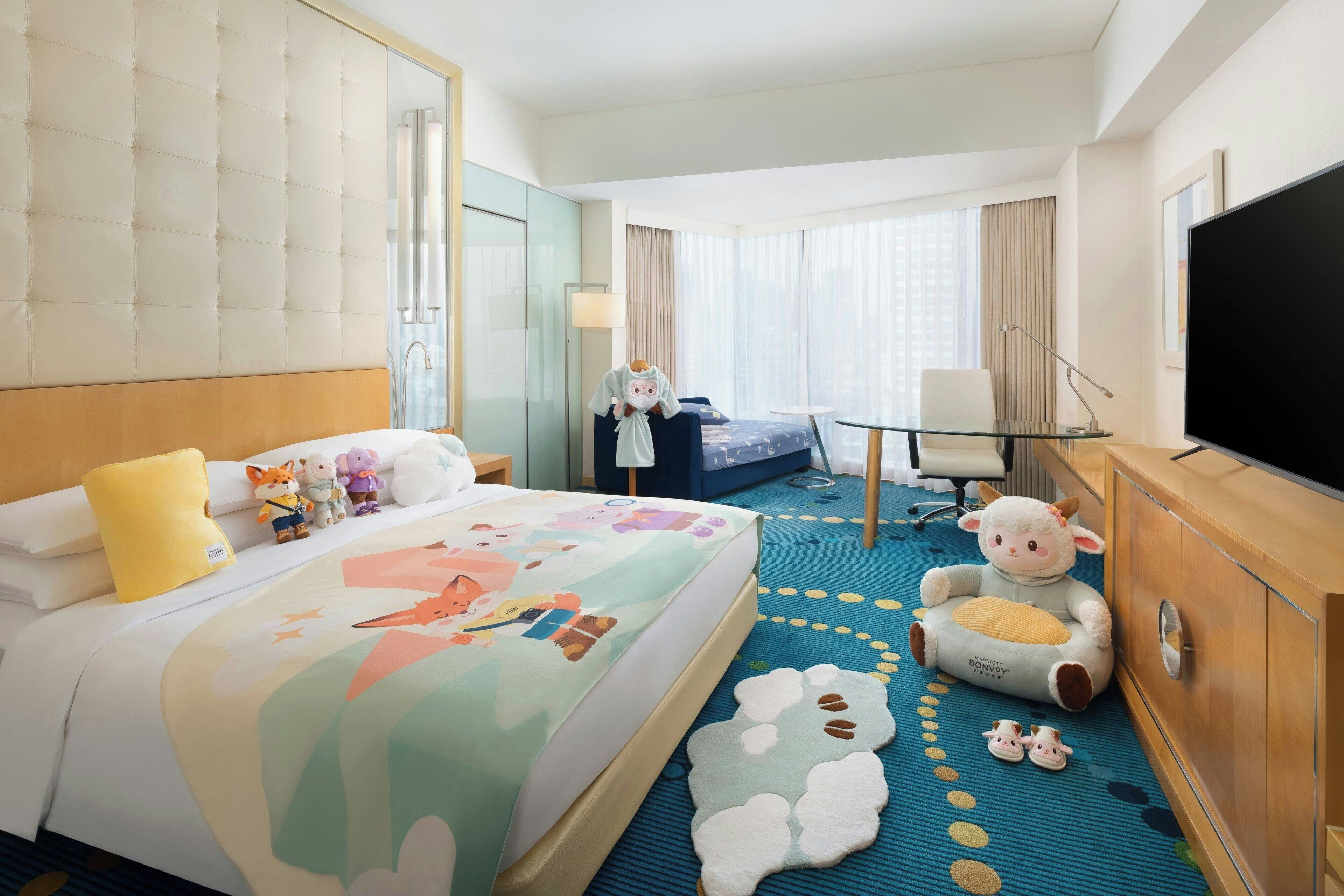 Una habitación de hotel con una cama grande, un escritorio, un televisor y juguetes de peluche.