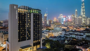 A modern hotel with a prominent 'R' logo, surrounded by a dense urban skyline with illuminated buildings. - Renaissance Shanghai Yu Garden Hotel on the Bund by Nanjing Road (Shanghai)