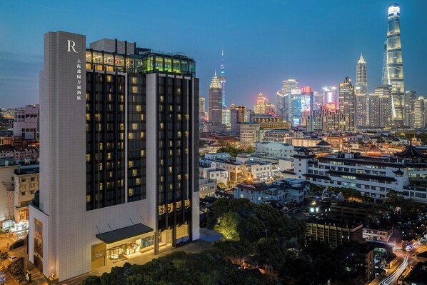 A modern hotel with a prominent 'R' logo, surrounded by a dense urban skyline with illuminated buildings.