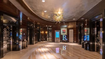 A modern hotel lobby with a polished marble floor, wooden paneling, and a central chandelier.