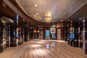 A modern hotel lobby with a polished marble floor, wooden paneling, and a central chandelier.