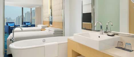 A modern hotel bathroom with two large tubs, a large mirror, and a city view.