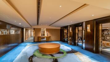 A spacious hallway with a central seating area, a reception desk, and a glass elevator.