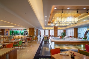 A modern hotel lobby with a central bar, multiple dining areas, and a staircase leading to an upper level.