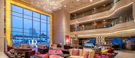 A spacious lobby with a large chandelier, comfortable seating, and a view of the cityscape through expansive windows.