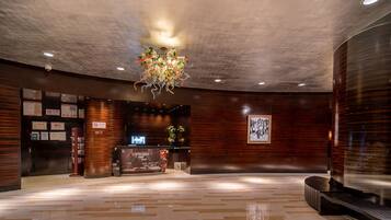 A lobby with a modern chandelier, wooden paneling, a reception desk, and a digital screen.