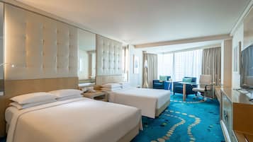 A hotel room with two beds, a desk, a chair, a TV, and a large window with curtains.