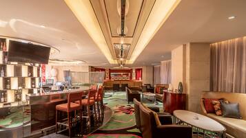 A modern hotel lobby with a bar area, seating, and a large TV screen.