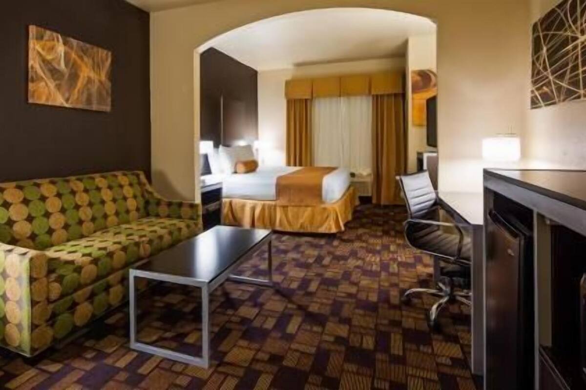 Habitación de hotel con un sofá estampado, una cama con cabecera, un escritorio y una silla.