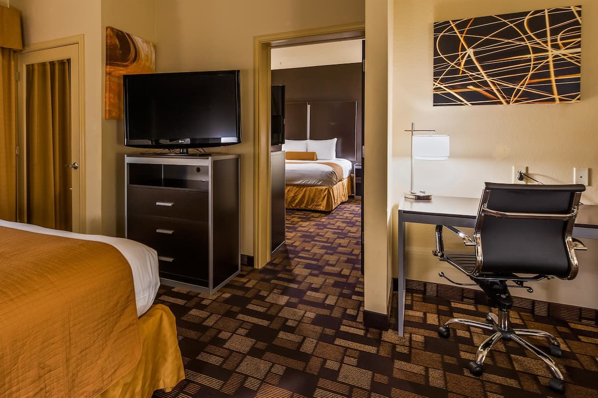 Habitación de hotel con cama, escritorio, silla, televisor y baño visible a través de una puerta abierta.