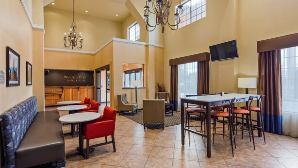 A hotel lobby with a reception desk, seating area, and a large dining table. - Best Western Windsor Pointe Hotel & Suites-Frost Bank Center (San Antonio)