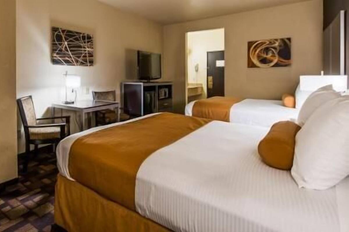 Habitación de hotel con dos camas, un escritorio, un televisor y obras de arte en las paredes.