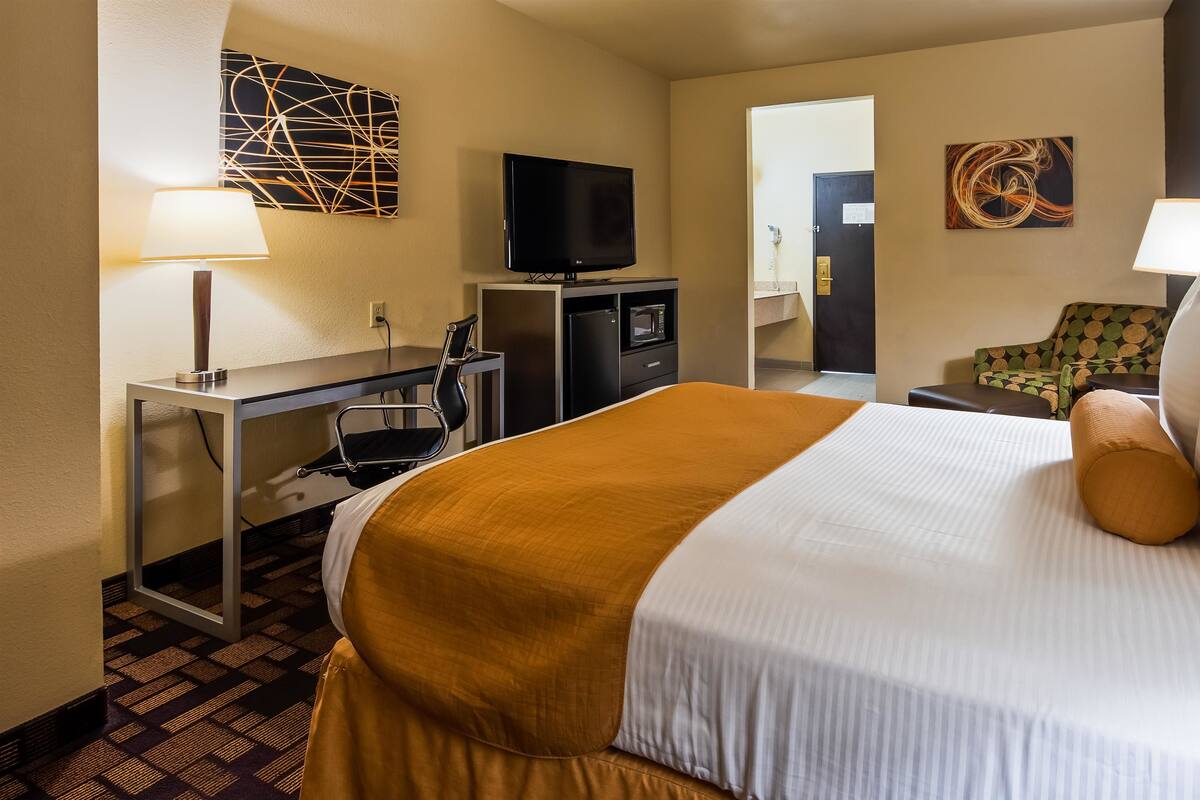 Habitación de hotel con cama, escritorio con silla, televisor y obras de arte en las paredes.