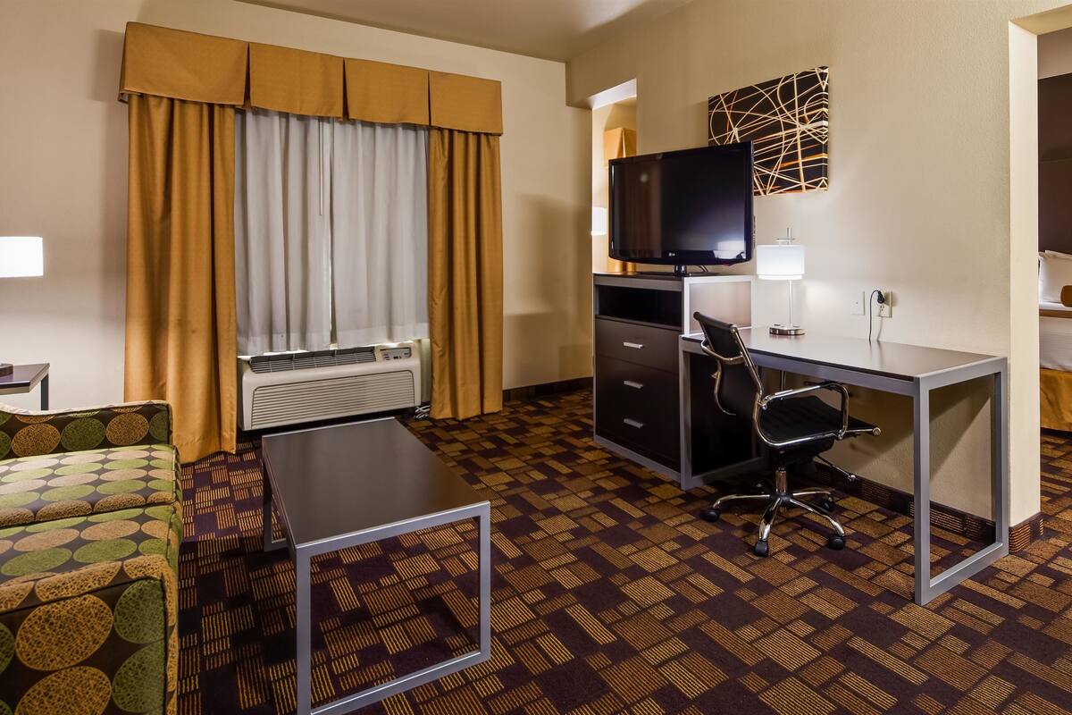 Habitación de hotel con cama, escritorio con silla, televisor, lámpara de escritorio y ventana con cortinas.