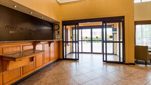 A hotel reception area with a reception desk, a clock, and a glass door leading outside. - Best Western Windsor Pointe Hotel & Suites-Frost Bank Center (San Antonio)