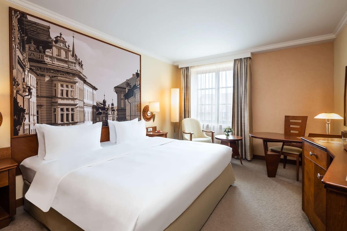 Habitación de hotel con una cama grande, un escritorio, una silla y vistas a la ciudad por la ventana.