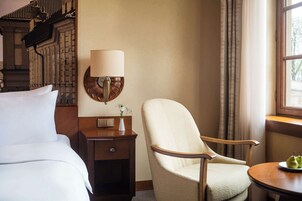 Een hotelkamer met een bed, een stoel, een nachtkastje met een lamp en een klein tafeltje met een schaal fruit.