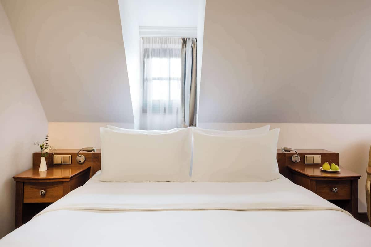 Una habitación de hotel con una cama grande, dos mesitas de noche, una silla y una ventana con cortinas.