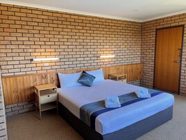 Una habitación de hotel con pared de ladrillo visto, cabecera de madera, cama con colcha azul y blanca, dos mesitas de noche con lámparas y una puerta de madera.
