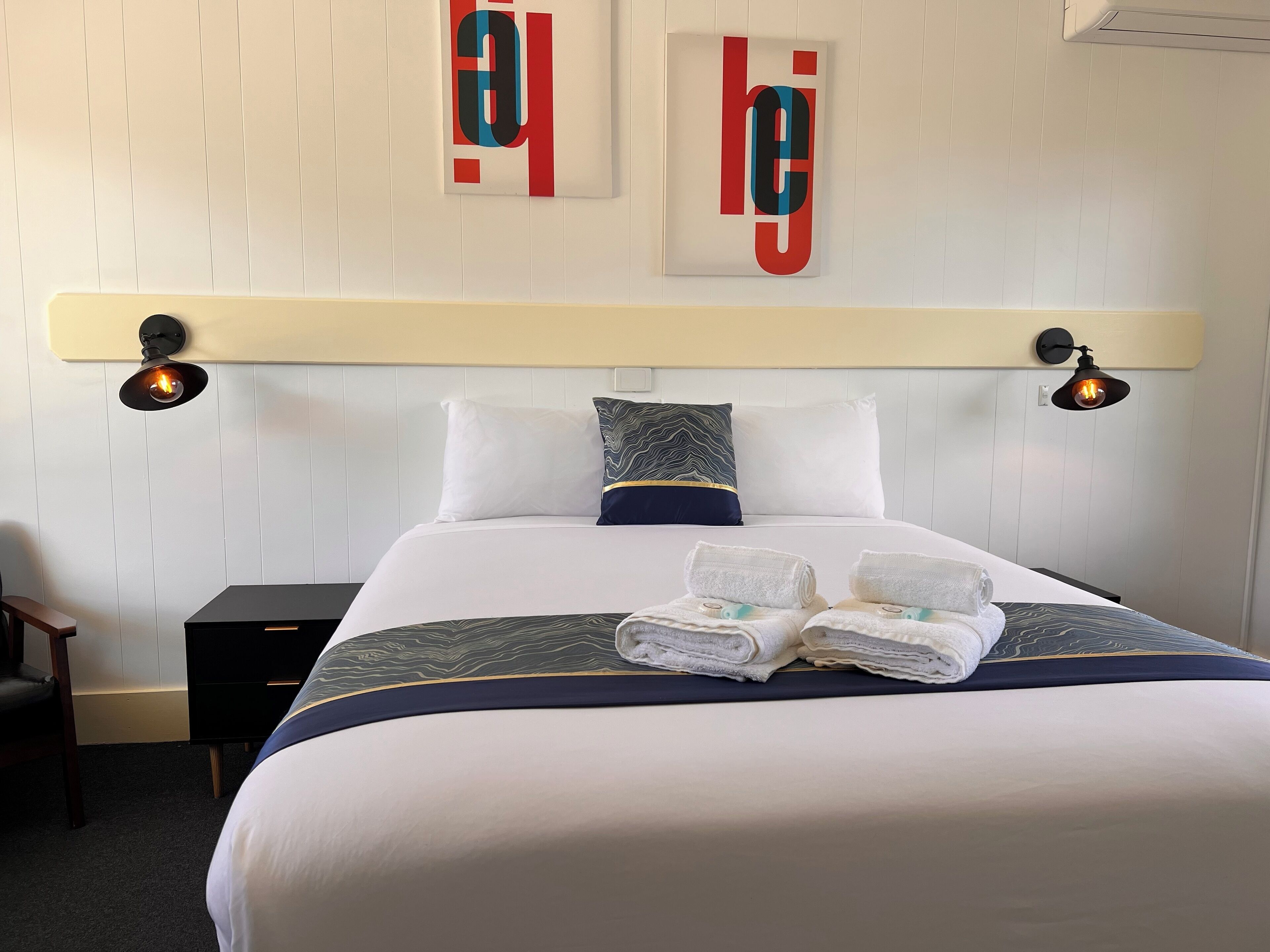 Una cama bien hecha con una colcha blanca y azul, dos almohadas y dos toallas dobladas sobre la cama.