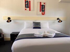 Una cama bien hecha con una colcha blanca y azul, dos almohadas y dos toallas dobladas sobre la cama.