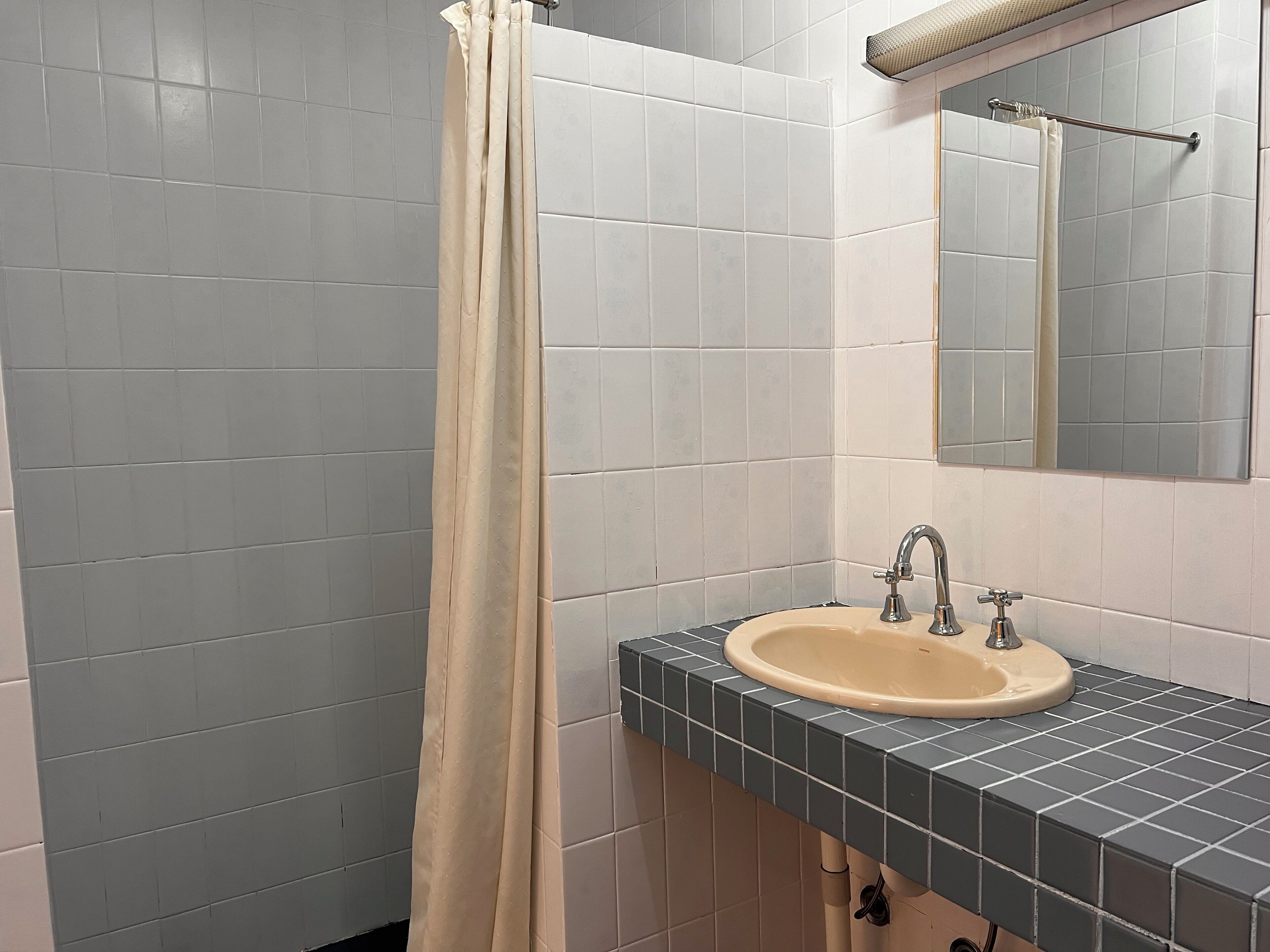 Une salle de bain avec un lavabo beige, un miroir au-dessus et un rideau de douche.