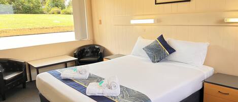 Habitación de hotel con cama, escritorio, silla y ventana con vista a zonas verdes.