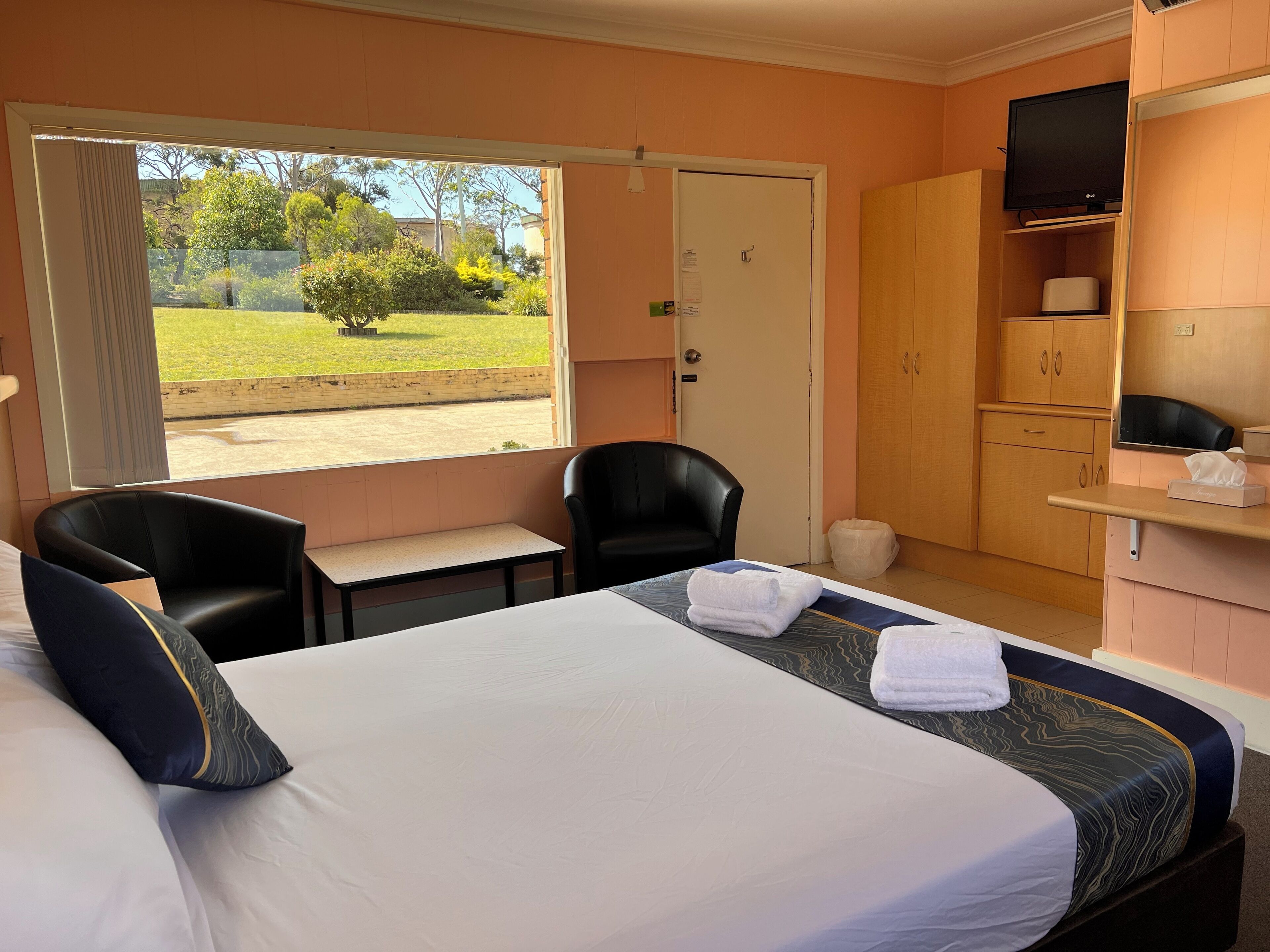 A hotel room with a bed, two chairs, a desk, a TV, and a wardrobe.
