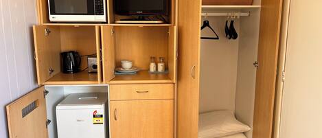 Una kitchenette compacta equipada con microondas, un refrigerador pequeño, cafetera y un televisor Samsung.