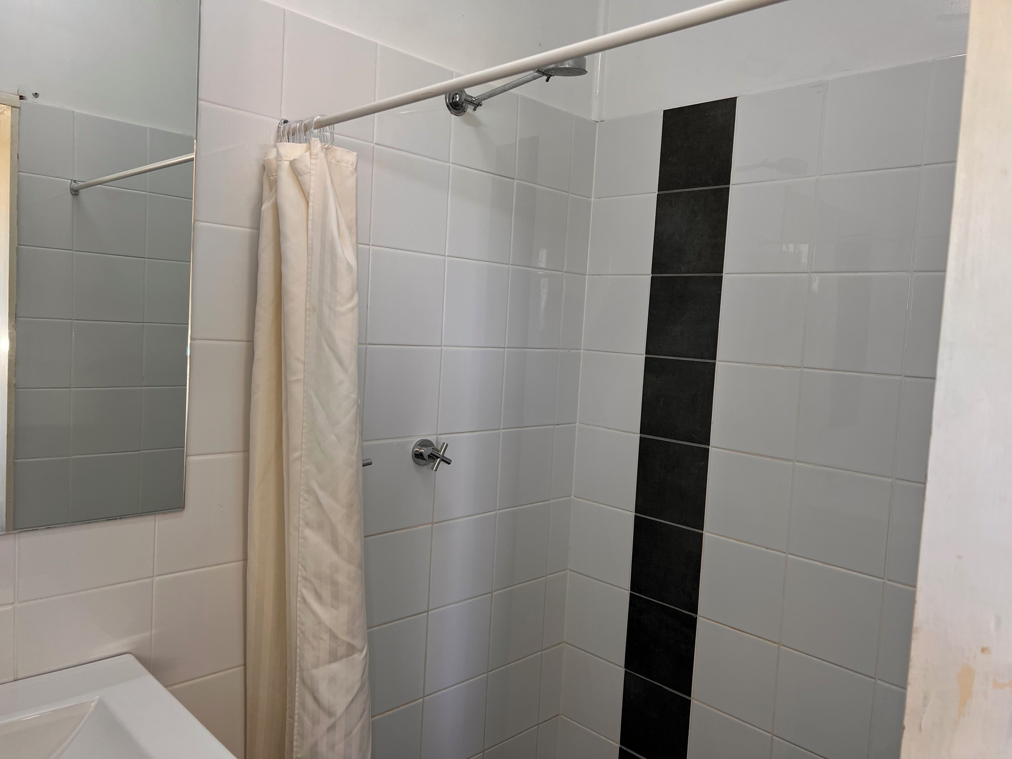 Ein Badezimmer mit weißen Fliesen, einer Dusche mit schwarzem vertikalem Streifen und einer Badewanne.