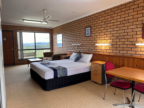 A hotel room with a large bed, a desk, a chair, a balcony with a view, and a brick wall.