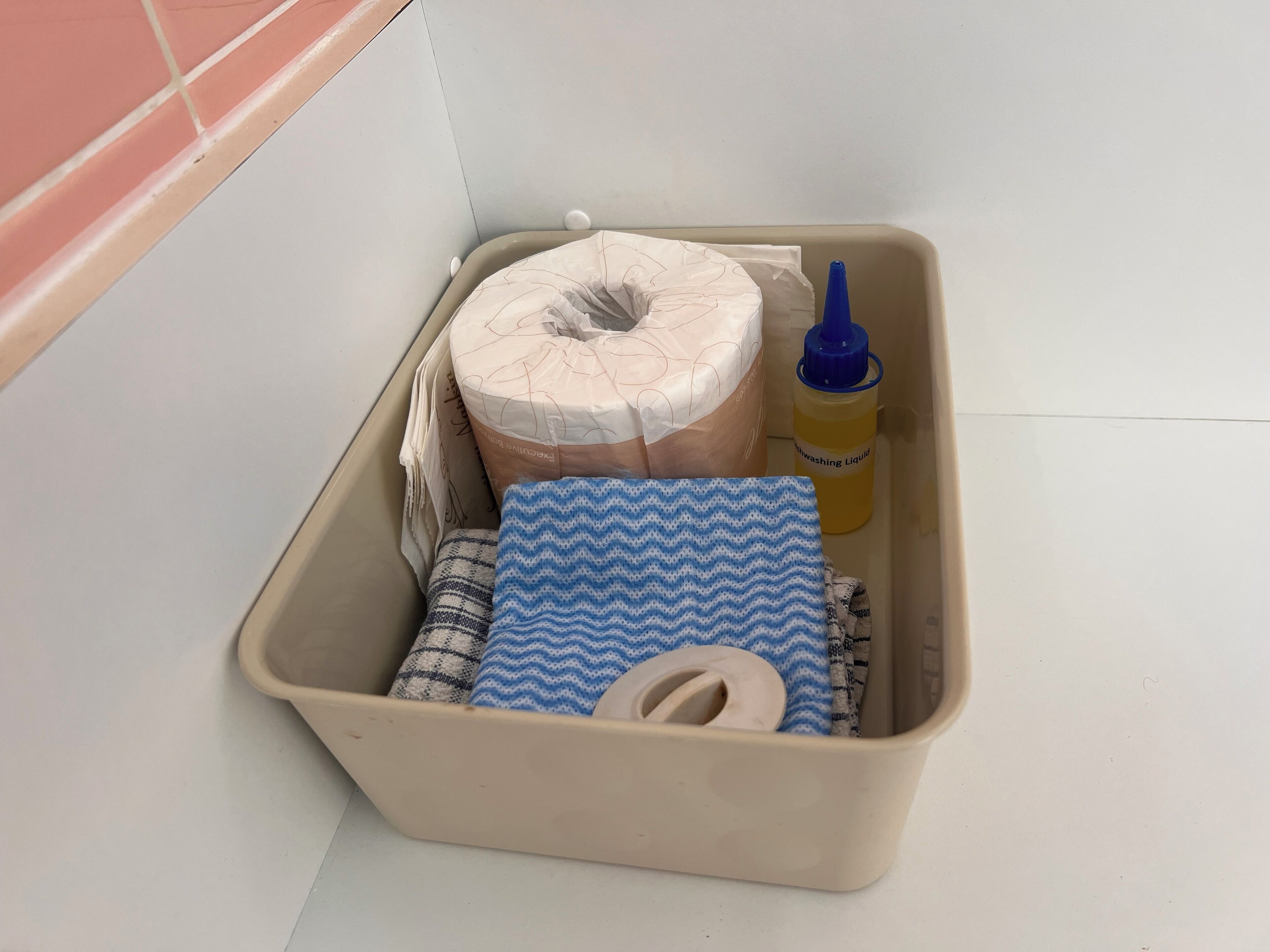 Un contenitore portaoggetti con un rotolo di carta igienica, un panno azzurro e bianco, una bottiglia di detersivo per il bucato e un sacchetto di carta.