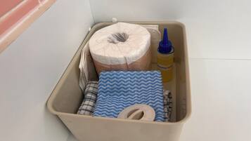 Un contenitore portaoggetti con un rotolo di carta igienica, un panno azzurro e bianco, una bottiglia di detersivo per il bucato e un sacchetto di carta.