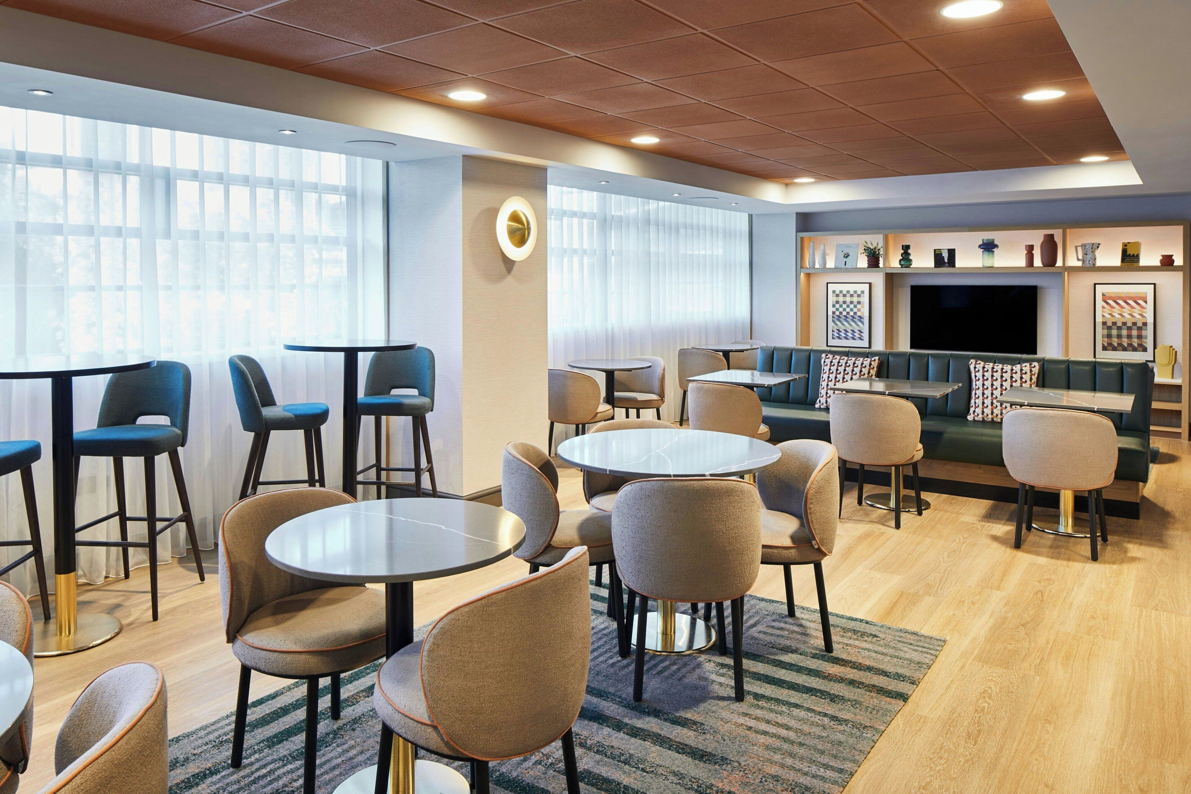 A modern lounge area with round tables and chairs, a sofa, and a TV screen.