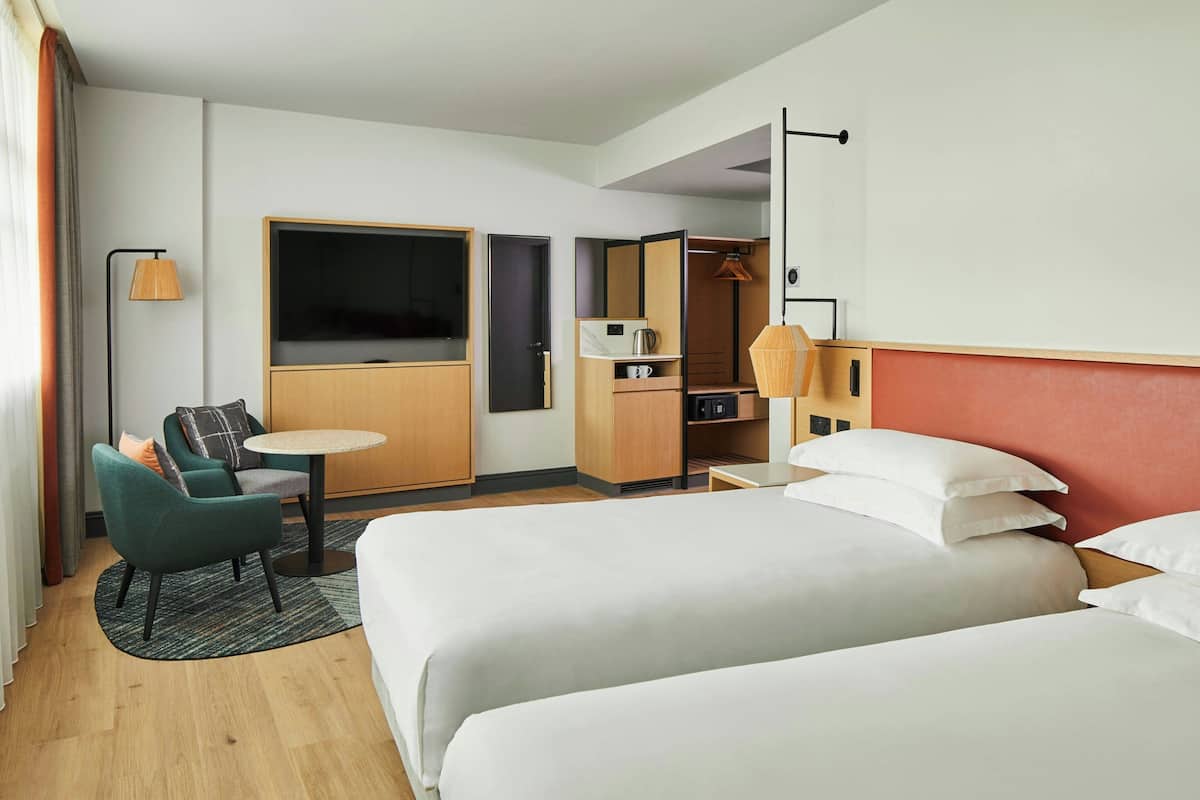 Ett hotellrum med två sängar, ett skrivbord, en stol, en TV och en garderob.