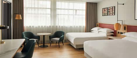 A hotel room with two beds, a desk, a chair, a small table, and a lamp.
