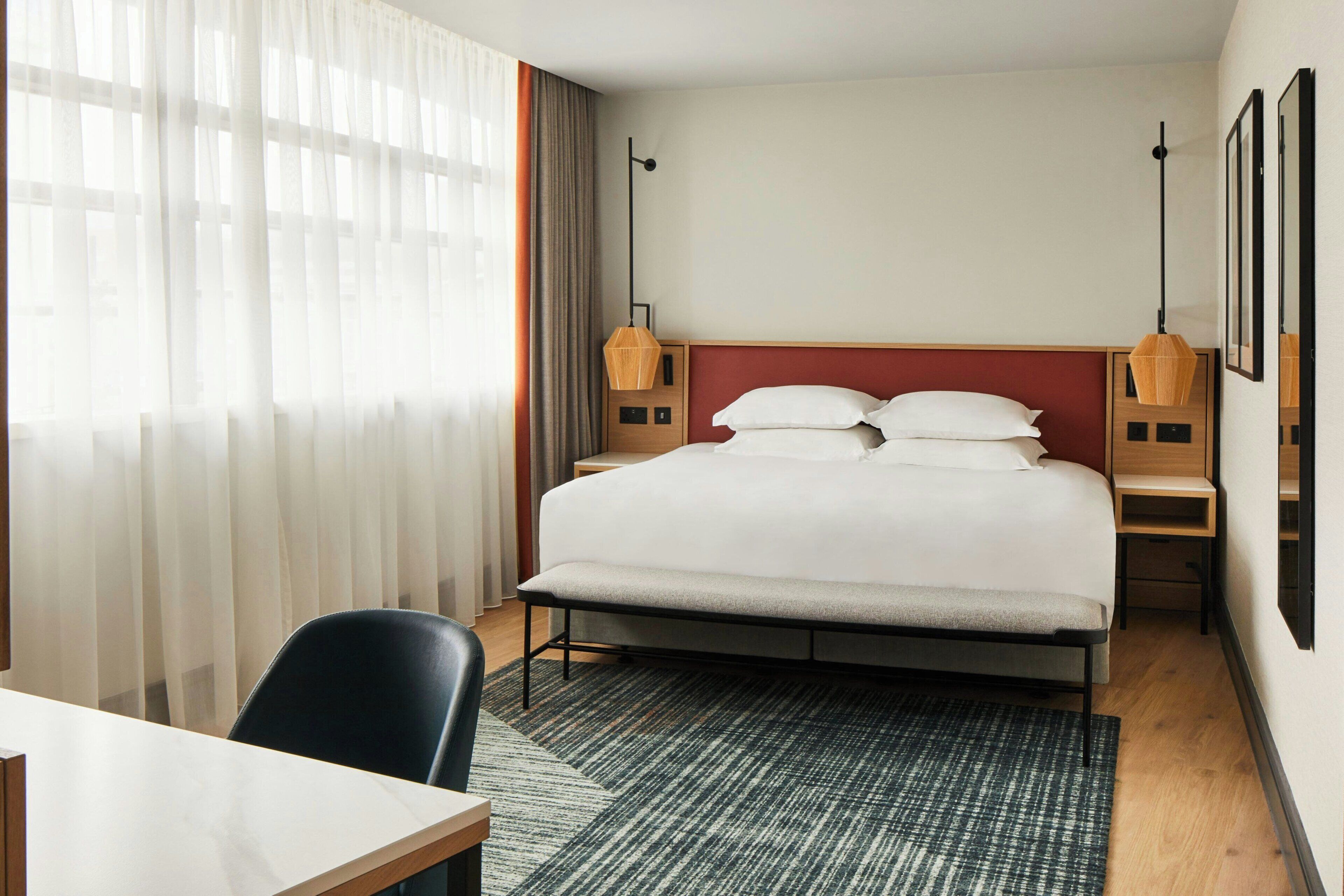 A hotel room with a large bed, a desk, and a chair. There are two bedside tables with lamps.
