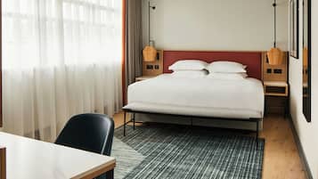 A hotel room with a large bed, a desk, and a chair. There are two bedside tables with lamps.