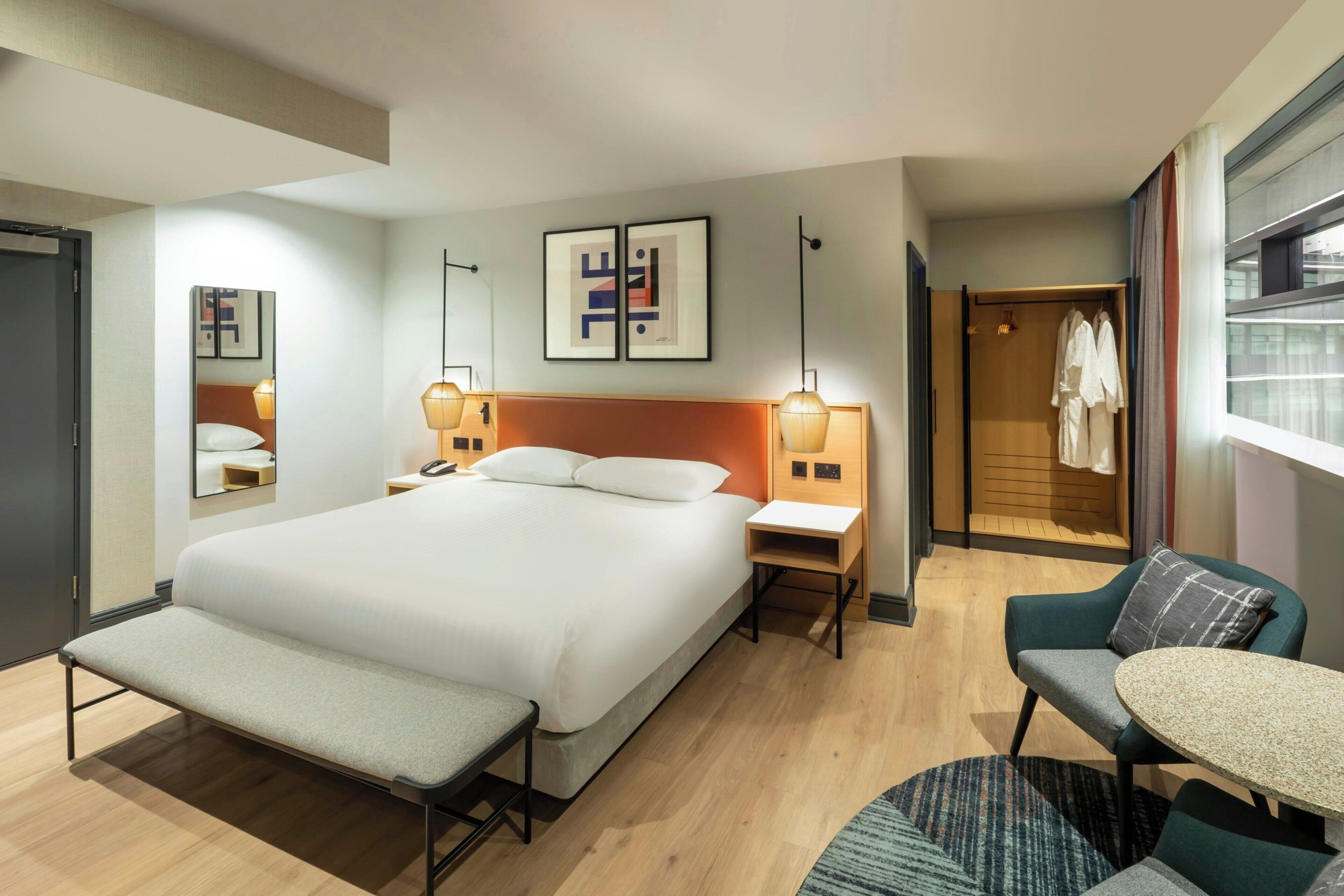 A hotel room with a large bed, bedside tables, a desk, a chair, a bench, and a wardrobe.