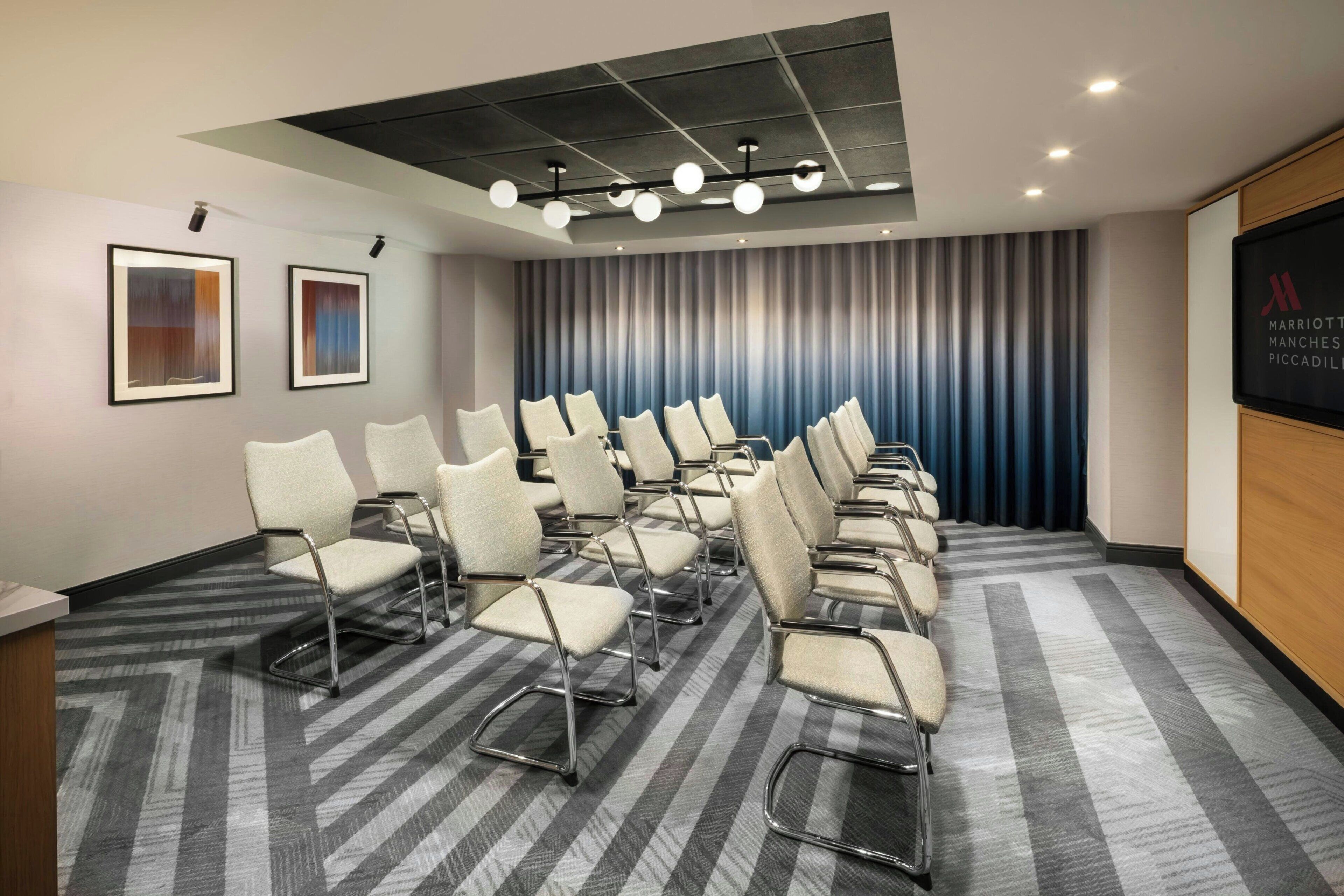 A conference room with rows of chairs, a projector screen, and a draped curtain.