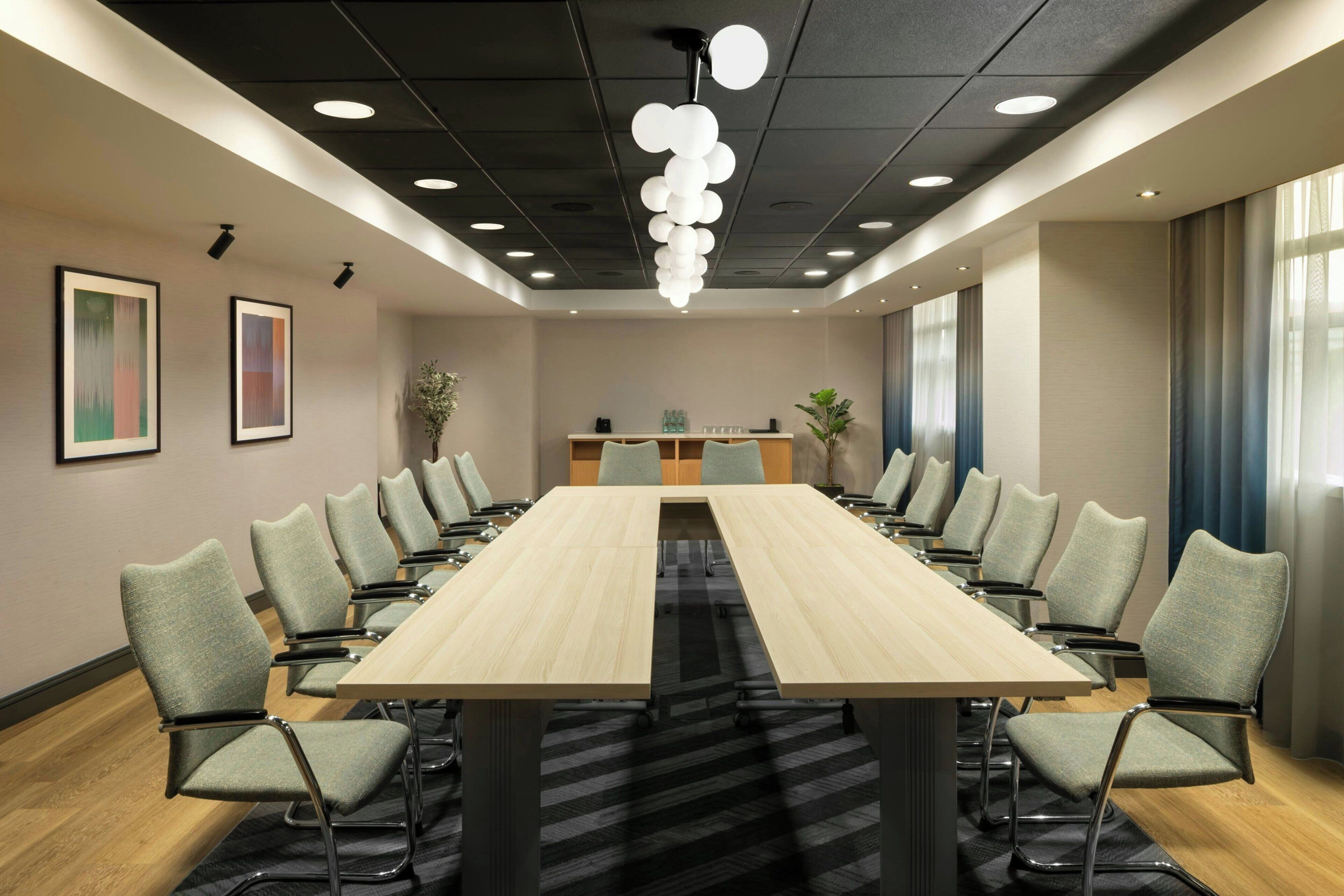 A conference room with a long table, chairs, a ceiling light fixture, and framed artwork on the wall.