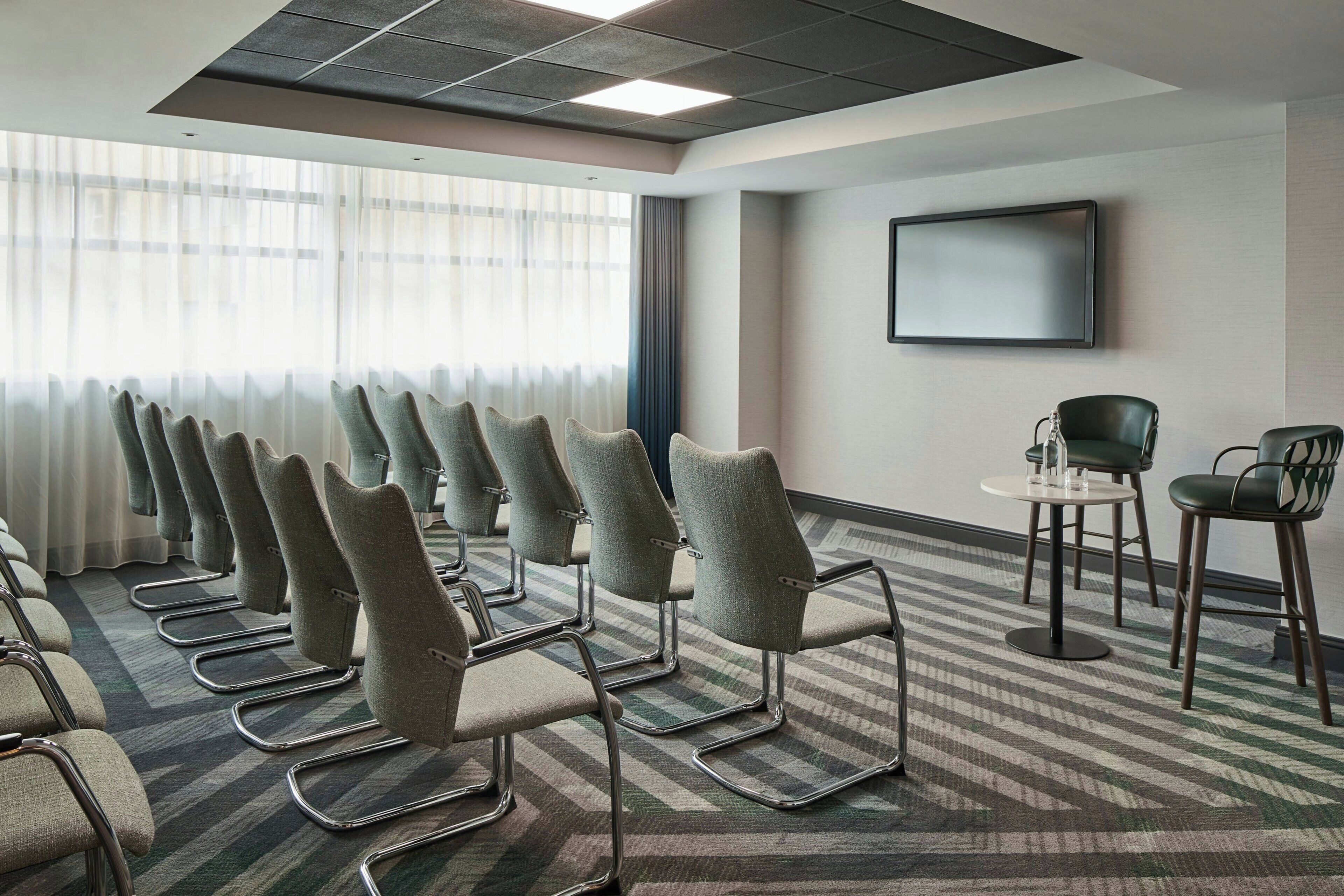 A conference room with rows of chairs, a television on the wall, and a patterned carpet.