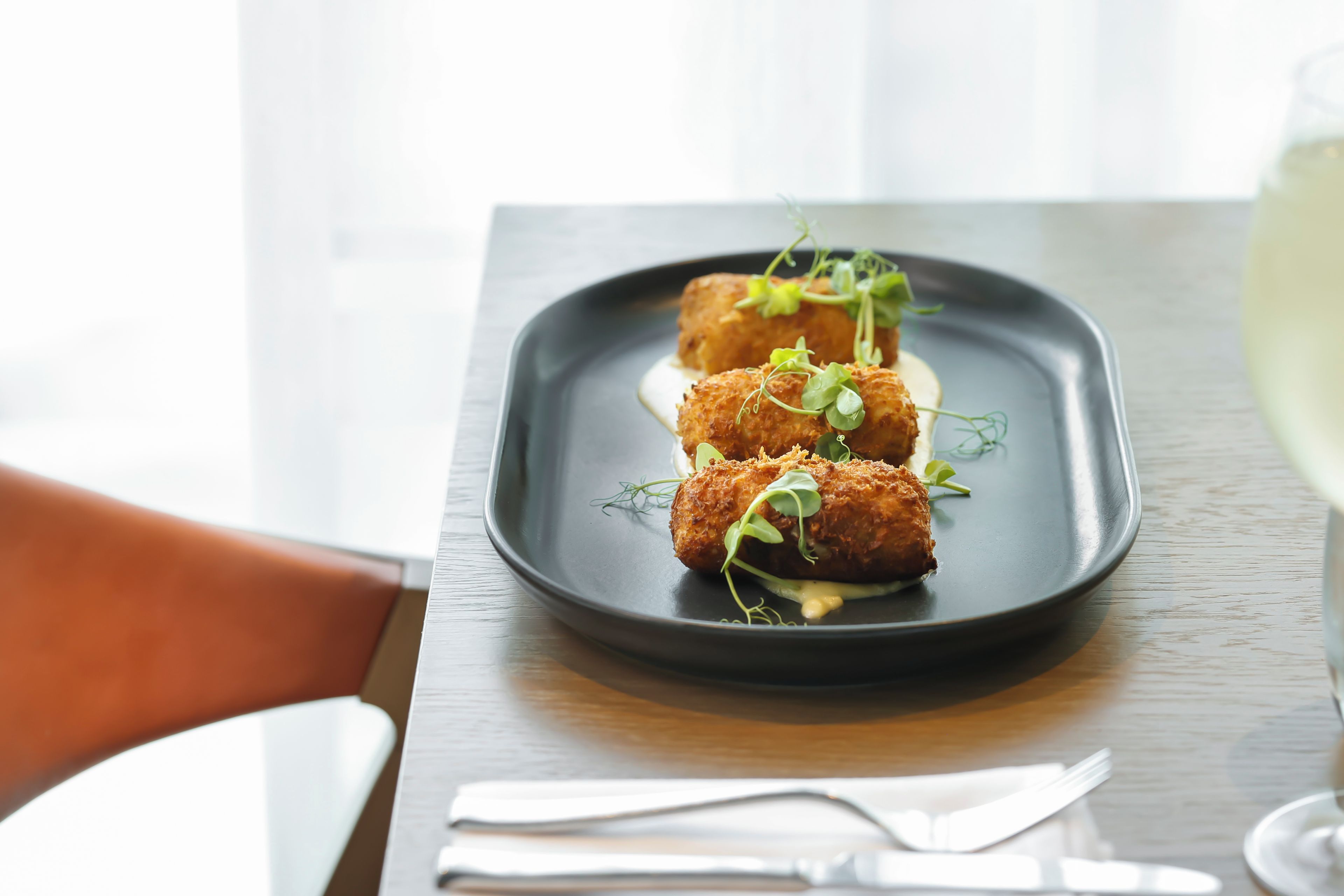 A rectangular plate with three golden-brown items, possibly fried food, garnished with green leaves, on a dark table.
