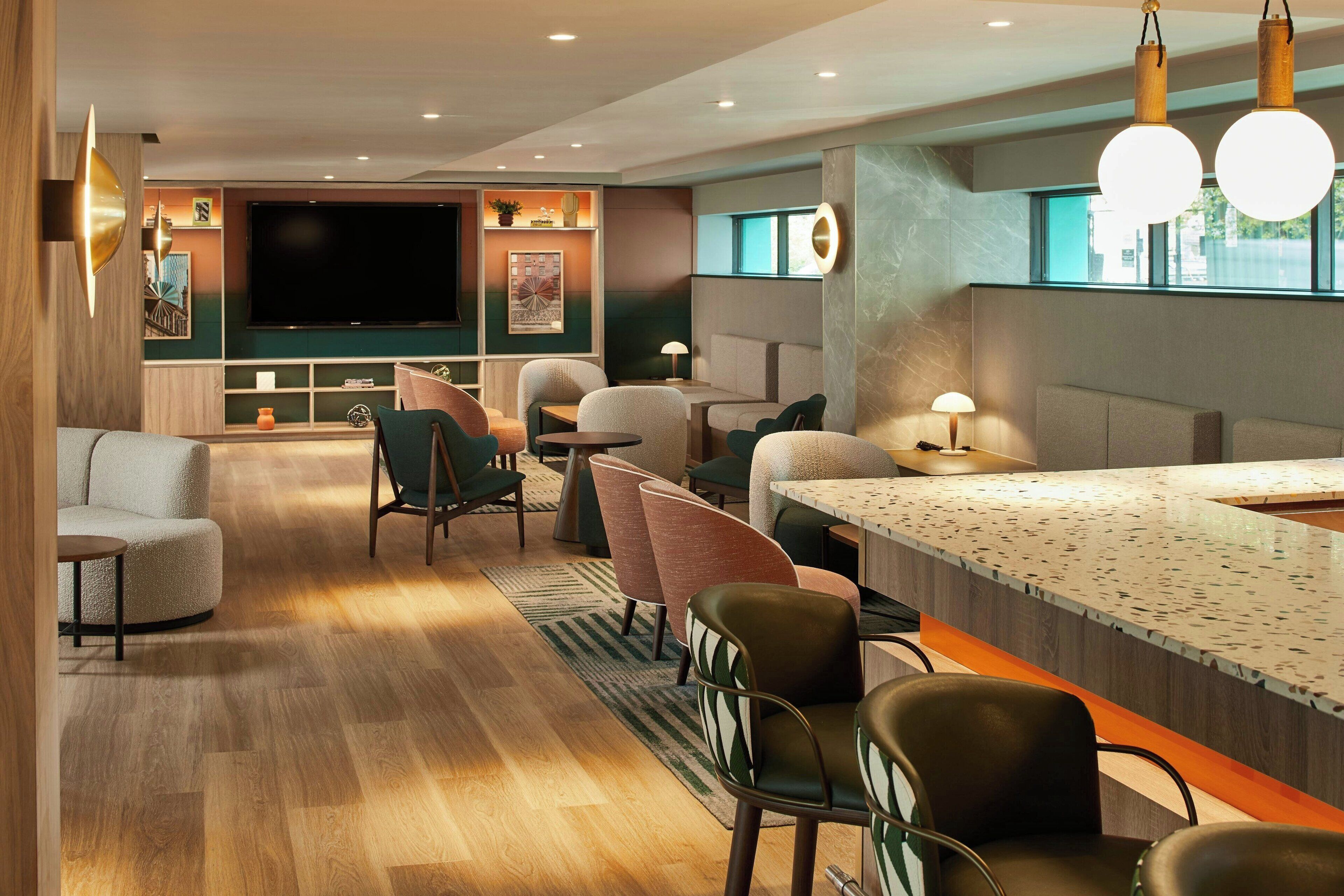 Un hall d’hôtel moderne doté d’un bar, de coins salon et d’un grand écran de télévision.